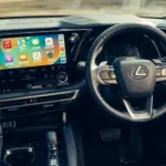 Lexus RX 450h+, cabine da versão internacional; volante, acabamento e equipamentos podem diferir no Brasil.